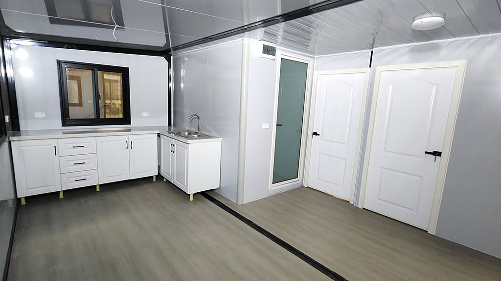 Interior view of a compact modular kitchen and living space with white cabinetry